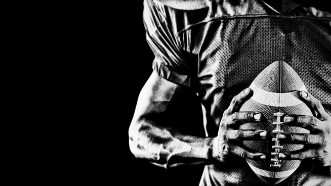 black and white image of football player holding football with black background