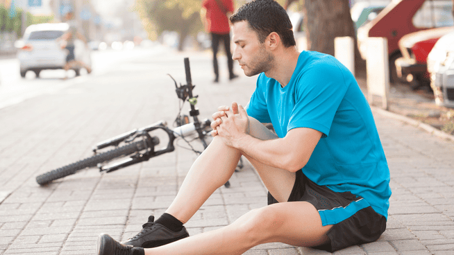 man holding injured knee with a potential acl injury while riding bike