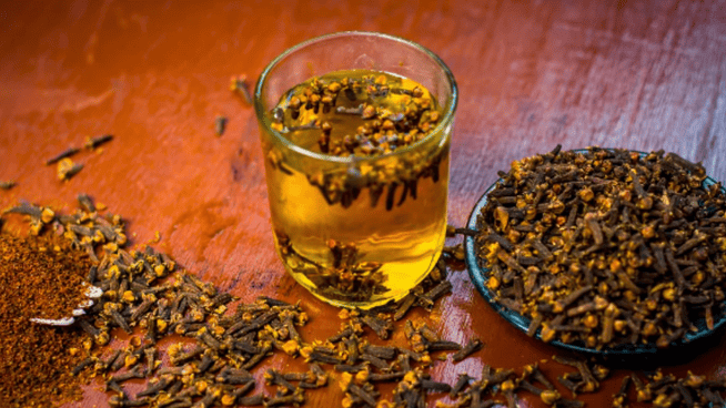 image of glass of clove water with cloves all over table