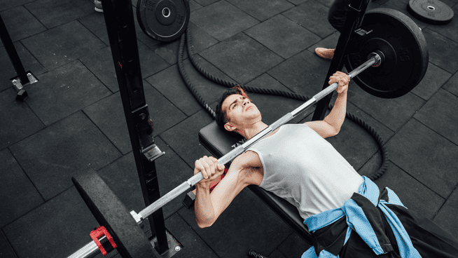 Athletic male performing bench press training in gym