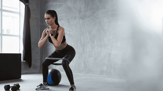 athletic woman performing squats with band in home