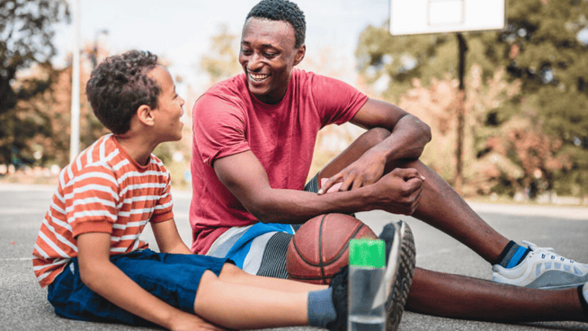 parent sitting with child while resting after playing basketball