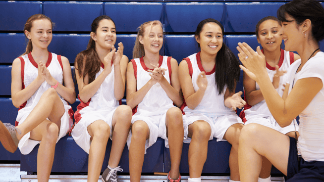 girls high school basketball coach in front of bench of high school basketball girls