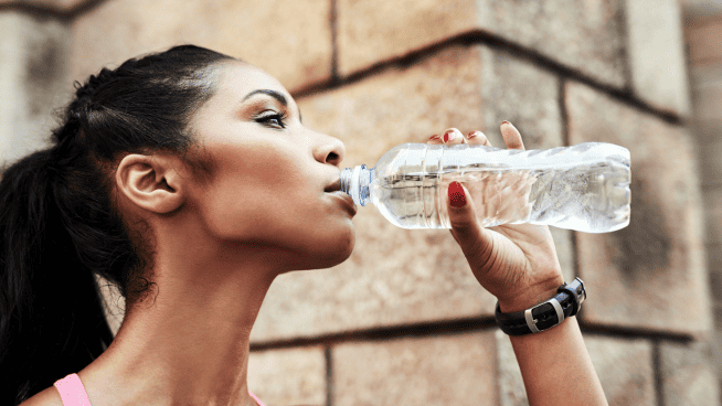 young female athlete drinking bottled water to stay hydrated