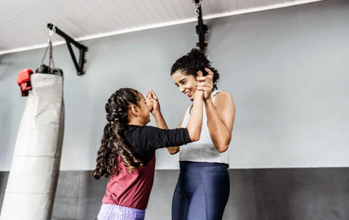 Mother celebrating with young daughter and female athlete at the gym during boxing training session